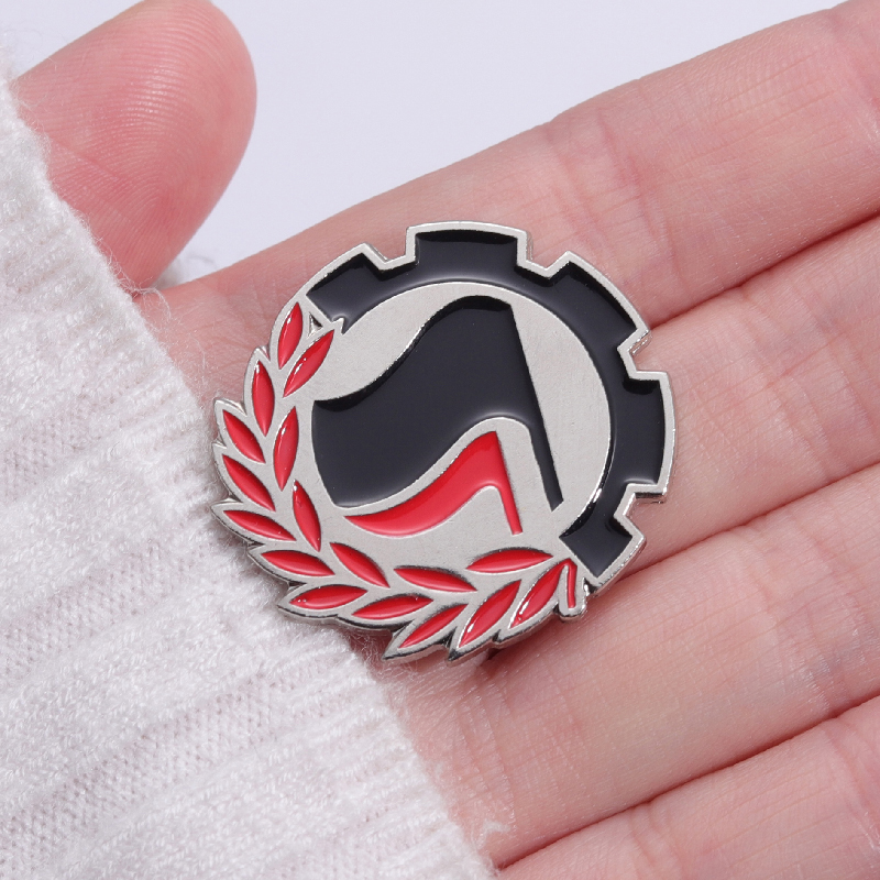 Pin antifasciste rouge et noir présenté dans la paume d’une main