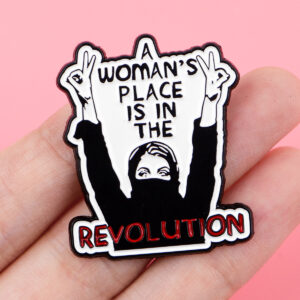 Pin féministe noir, blanc et rouge tenu entre les doigts