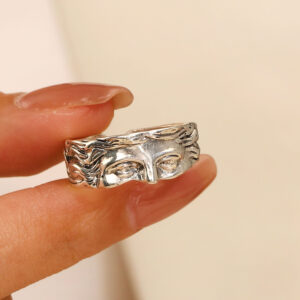 Bague visage de Vénus argentée tenue entre les doigts