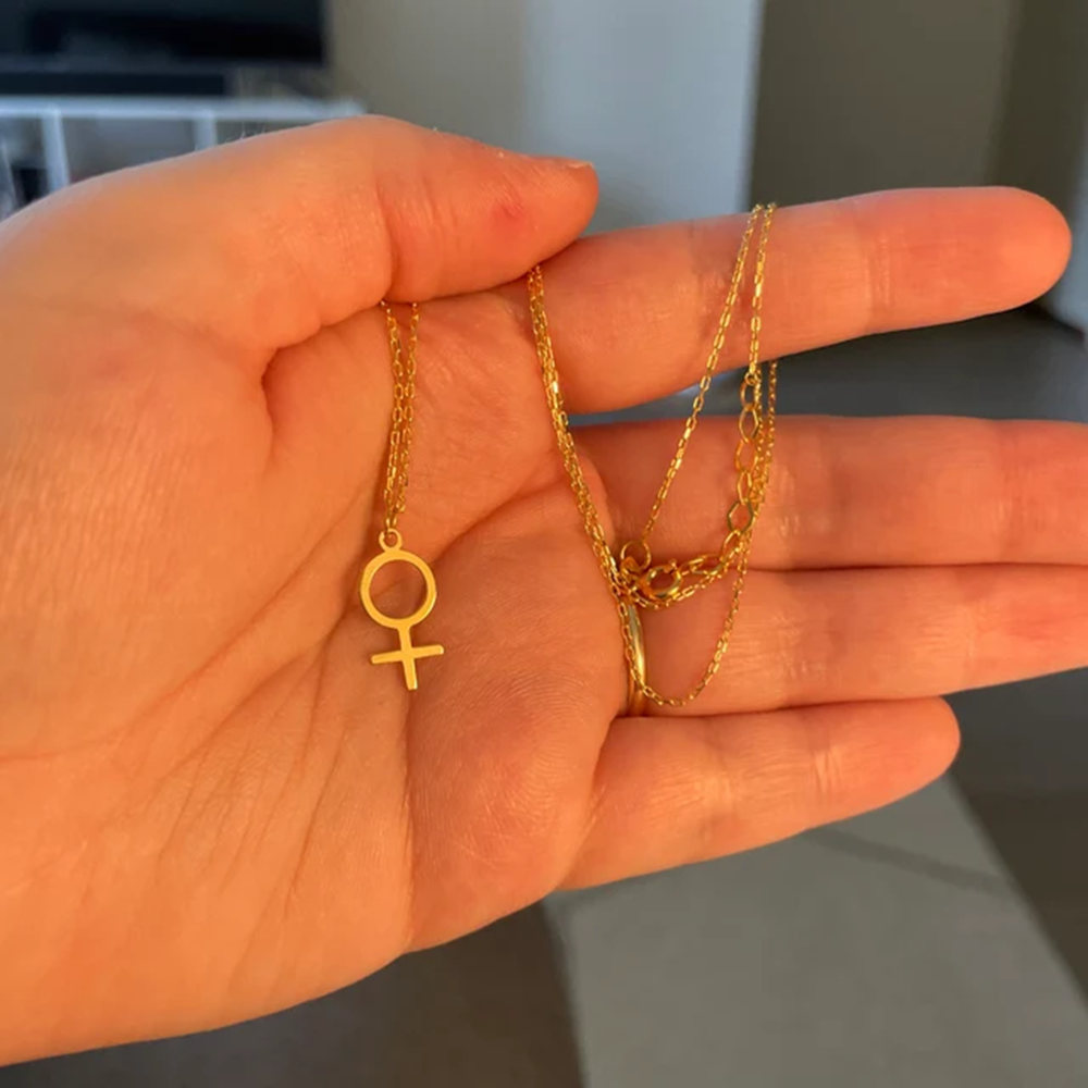 Pendentif Vénus doré tenu dans une main