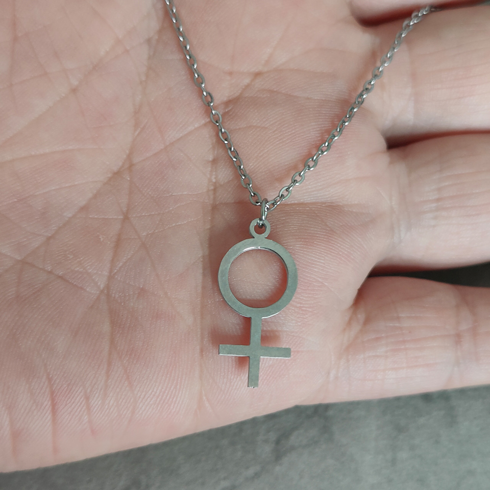 Collier féministe argenté tenu dans une main